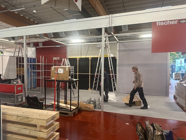 Aufbau des fischer Messestands in der Halle mit Leitern, Werkzeug und Standmaterial
